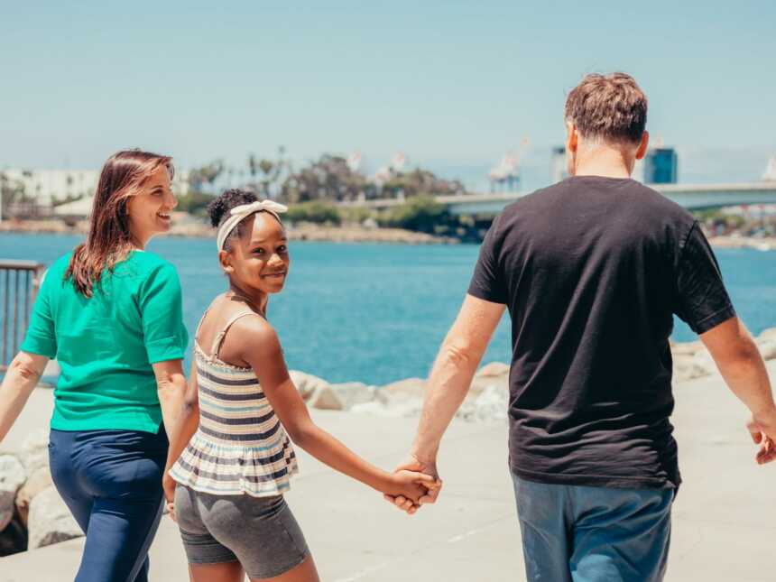 a teen girl walks hand in hand with her adoptive parents on the beach